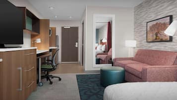 A hotel room with a bed, a desk with a computer, a TV, and a sofa.