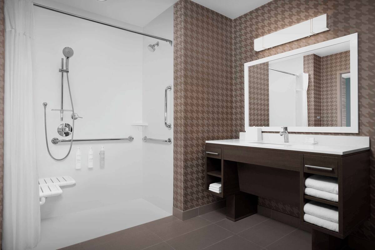 Ein modernes Badezimmer mit barrierefreier Dusche, einem Waschtisch mit großem Spiegel und einem Handtuchhalter.