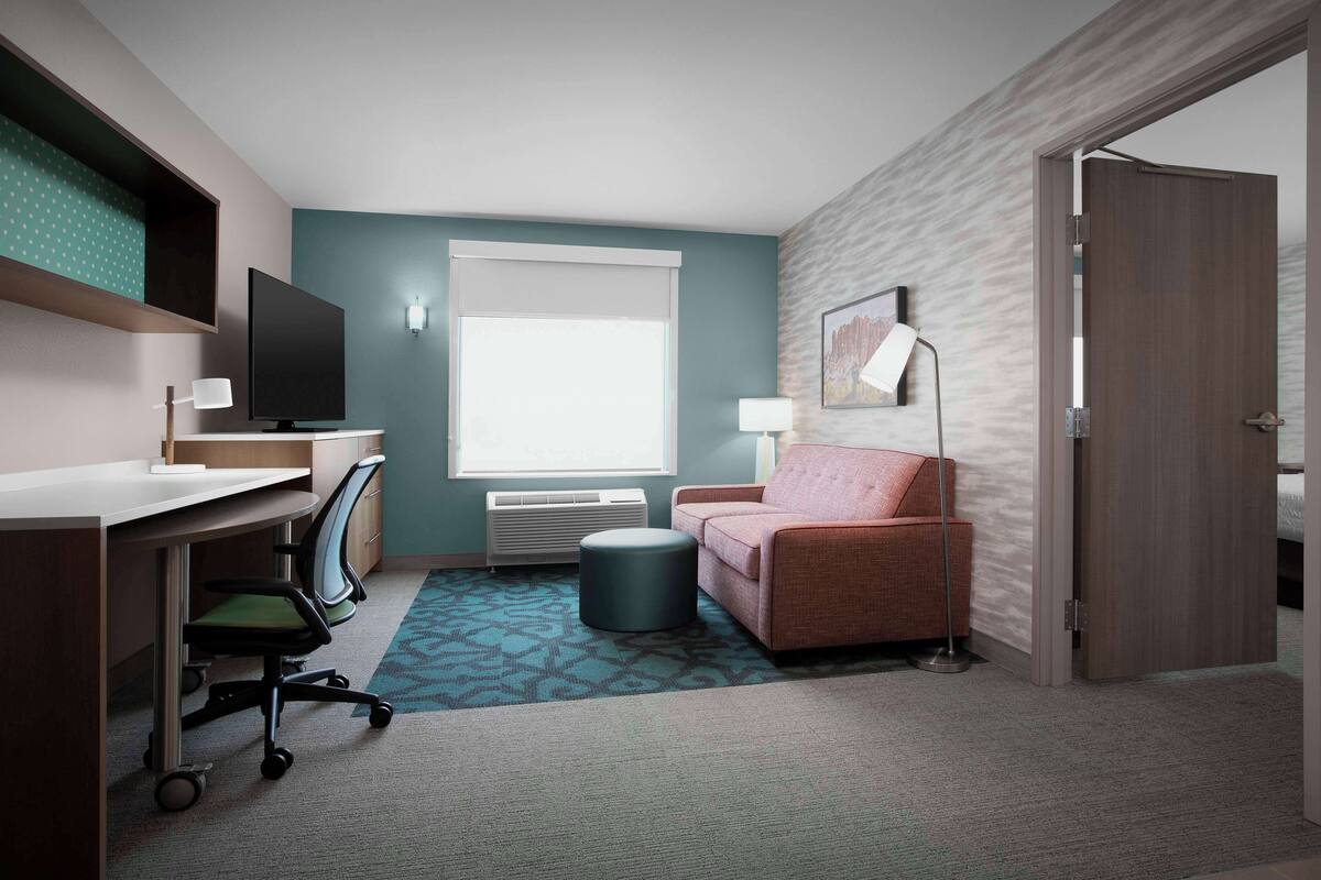 Ein Hotelzimmer mit Schreibtisch, Stuhl, Sofa und einem großen Fenster.
