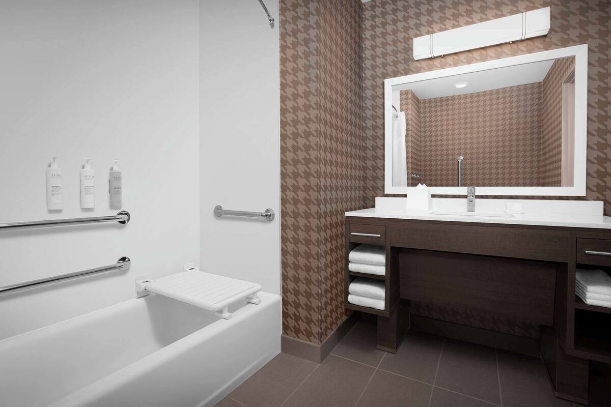 Ein modernes Badezimmer mit einer Badewanne, einem Waschtisch inklusive Spiegel und einem Handtuchhalter.