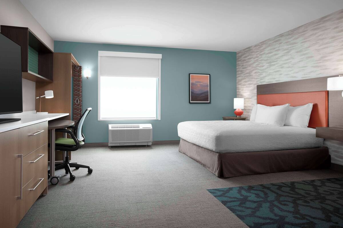 Ein Hotelzimmer mit Bett, Schreibtisch, Stuhl und einem Fenster mit Jalousien.