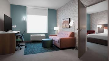 Una habitación de hotel con escritorio, silla, sofá, otoman y cama.
