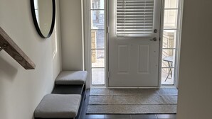 Un hall d’entrée propre et moderne, avec un banc, un miroir et une porte donnant sur un espace extérieur.