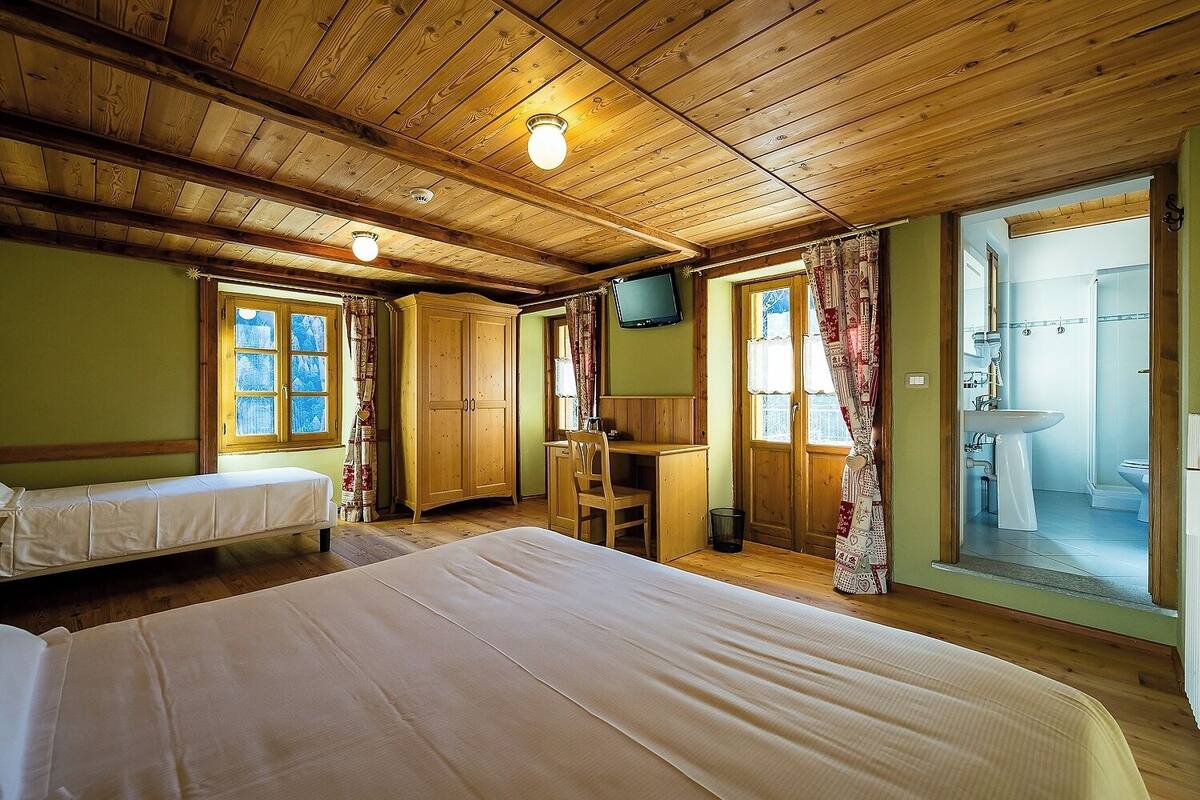 A room with two beds, a desk, a television, and a bathroom visible through an open door.