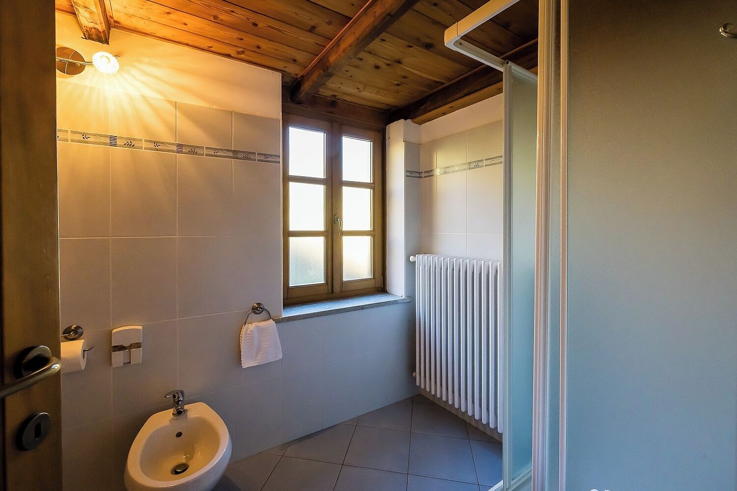 A bathroom with a bidet, a window, and a radiator.