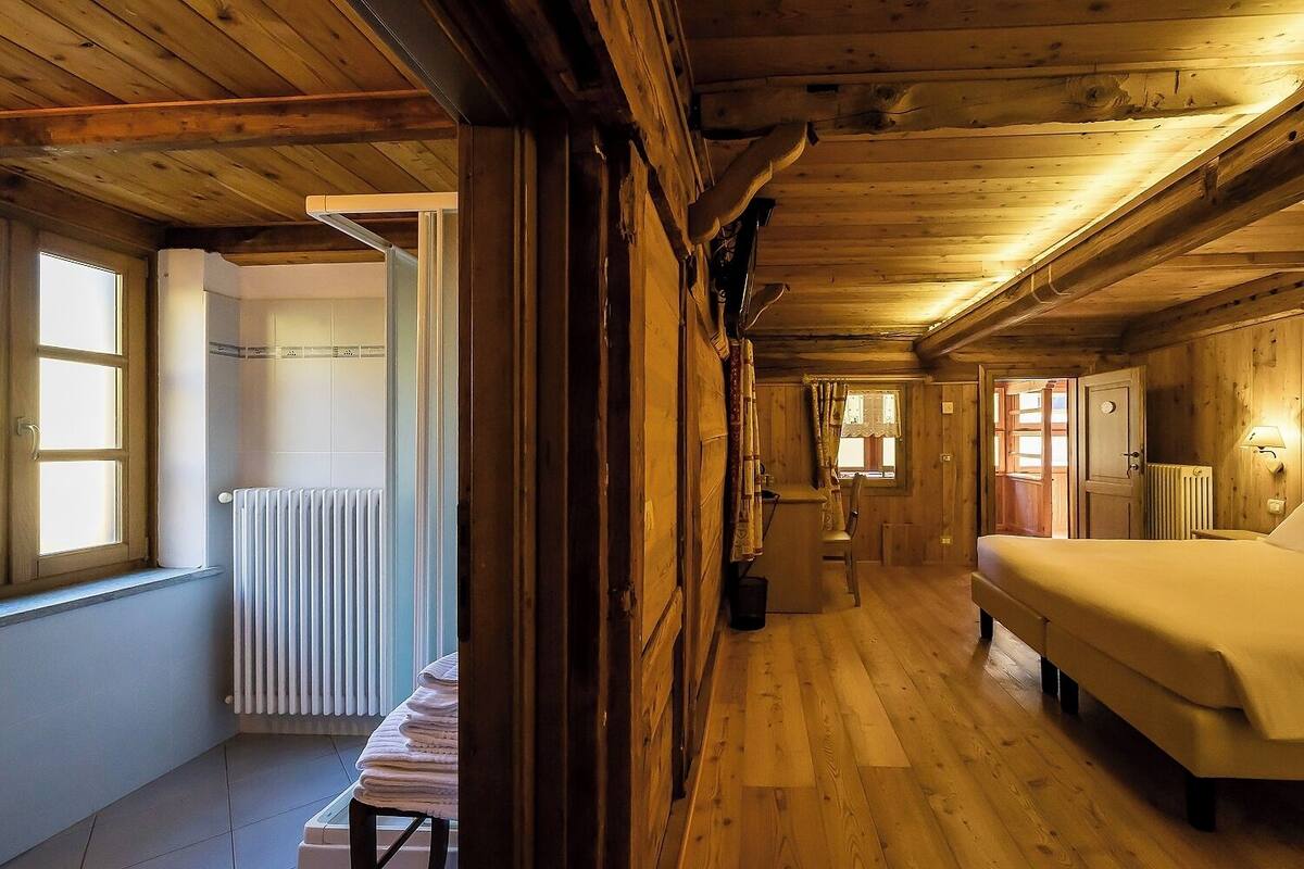 A wooden cabin interior with a bed, a radiator, and a window.