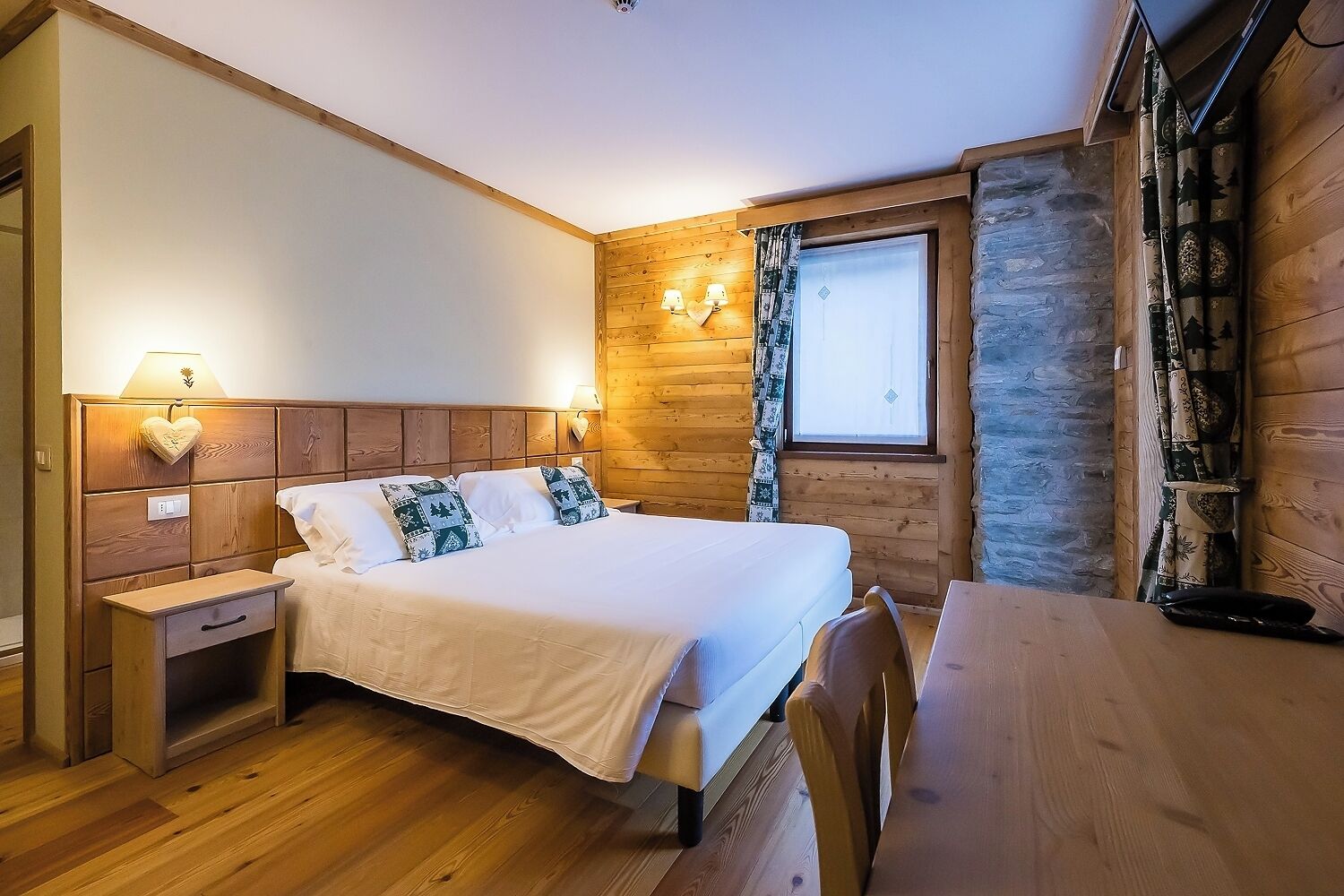 A cozy wooden cabin room with a bed, bedside table, lamp, and a window with curtains.
