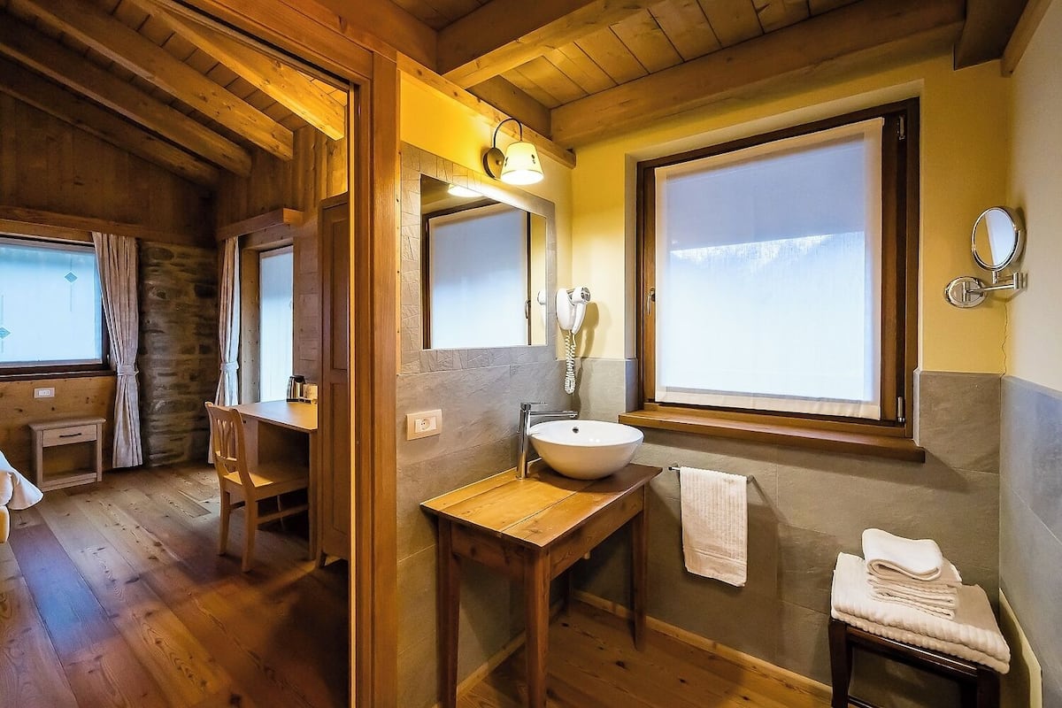 A wooden cabin bathroom with a wooden vanity, a large mirror, a sink, and a window with a view of the mountains.