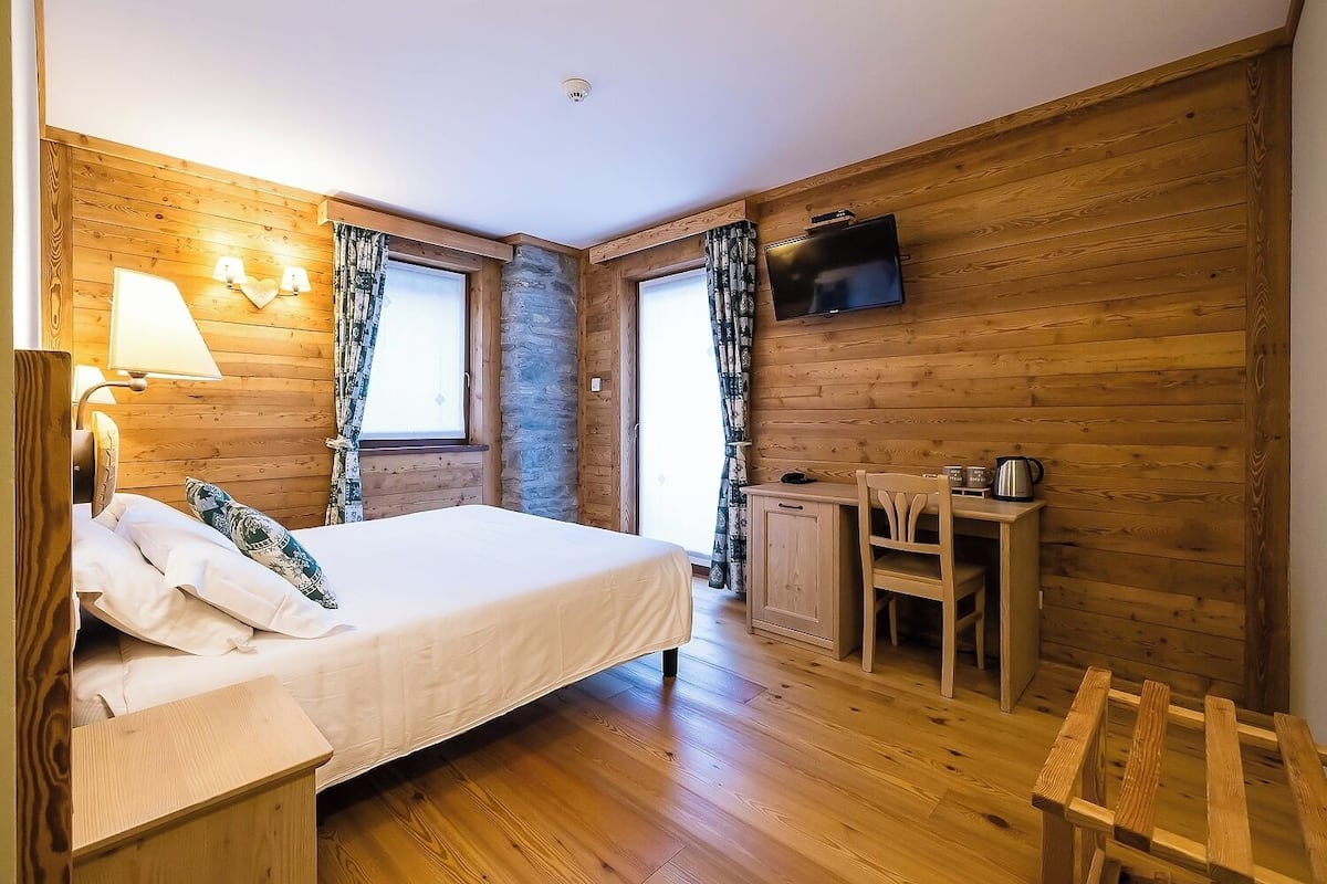 A wooden-paneled room with a bed, a desk, a chair, and a TV.