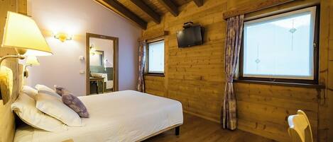 A wooden cabin bedroom with a bed, a nightstand, a lamp, a mirror, a sink, and a window with curtains.