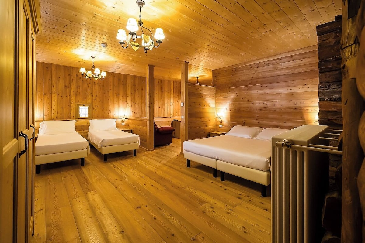 A cozy wooden cabin room with two beds, a wooden ceiling, and a central chandelier.