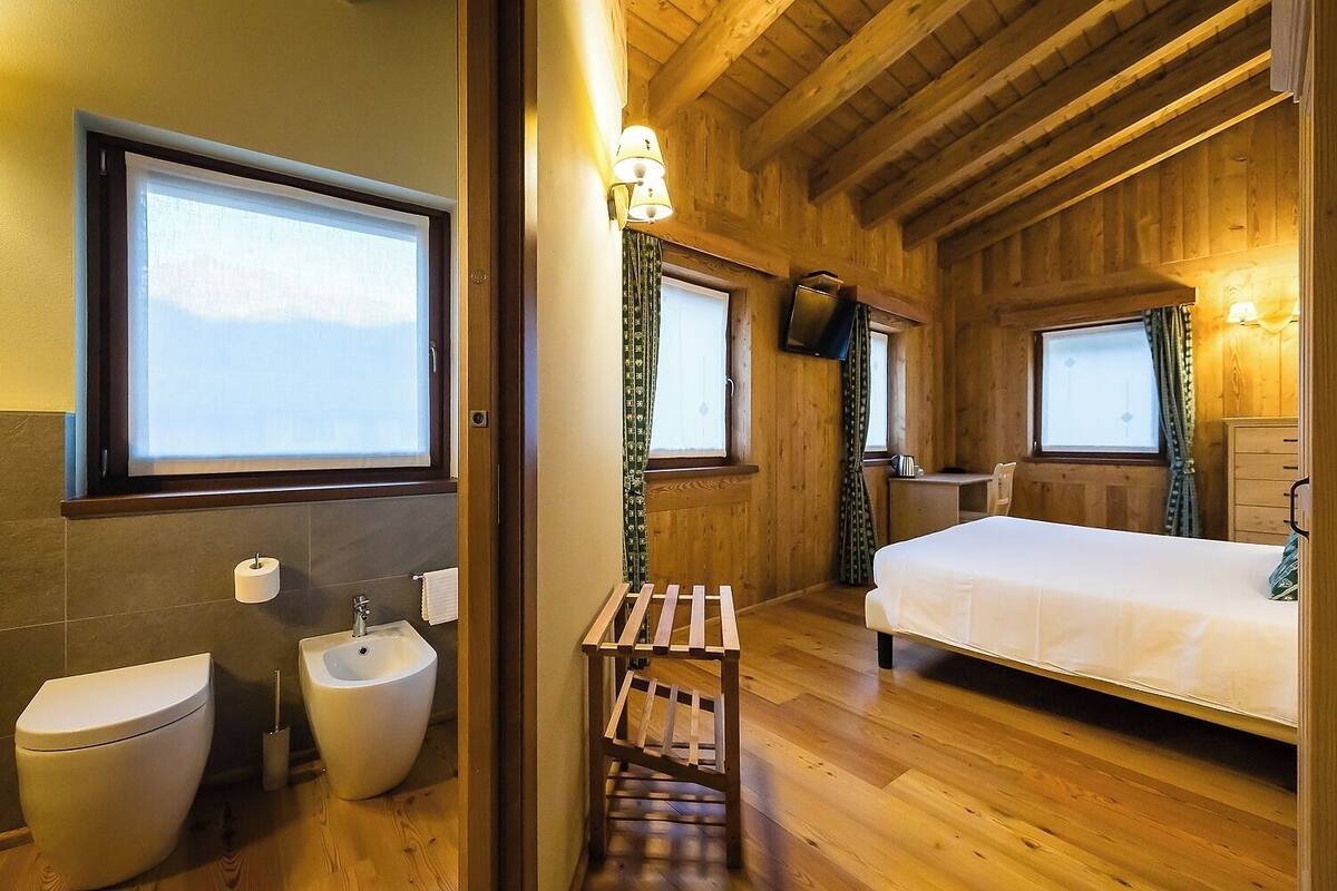 A wooden cabin room with a bed, a small table, a sink, and a toilet.
