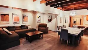 Un salon moderne avec un canapé, une table basse et un coin repas. Des tableaux encadrés ornent le mur, et on aperçoit une cuisine au fond.