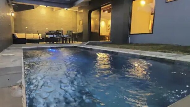Une piscine intérieure avec une terrasse carrelée et une table entourée de chaises à l’arrière-plan.