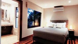 Une chambre avec un grand lit, une fenêtre donnant sur la verdure, une baignoire intégrée et une table de chevet avec une lampe.