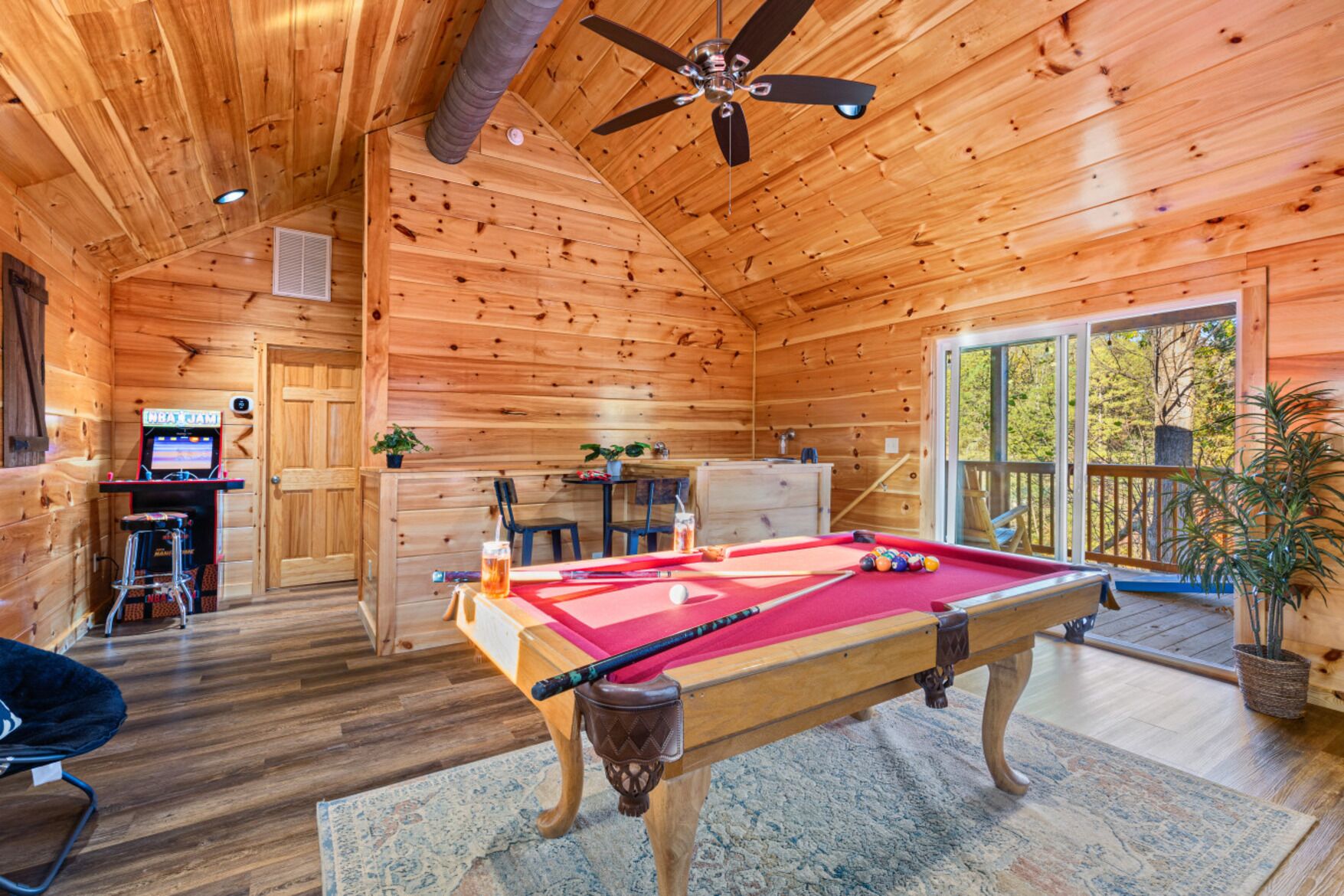 A wooden cabin interior with a pool table, a bar area, and a balcony with a view.