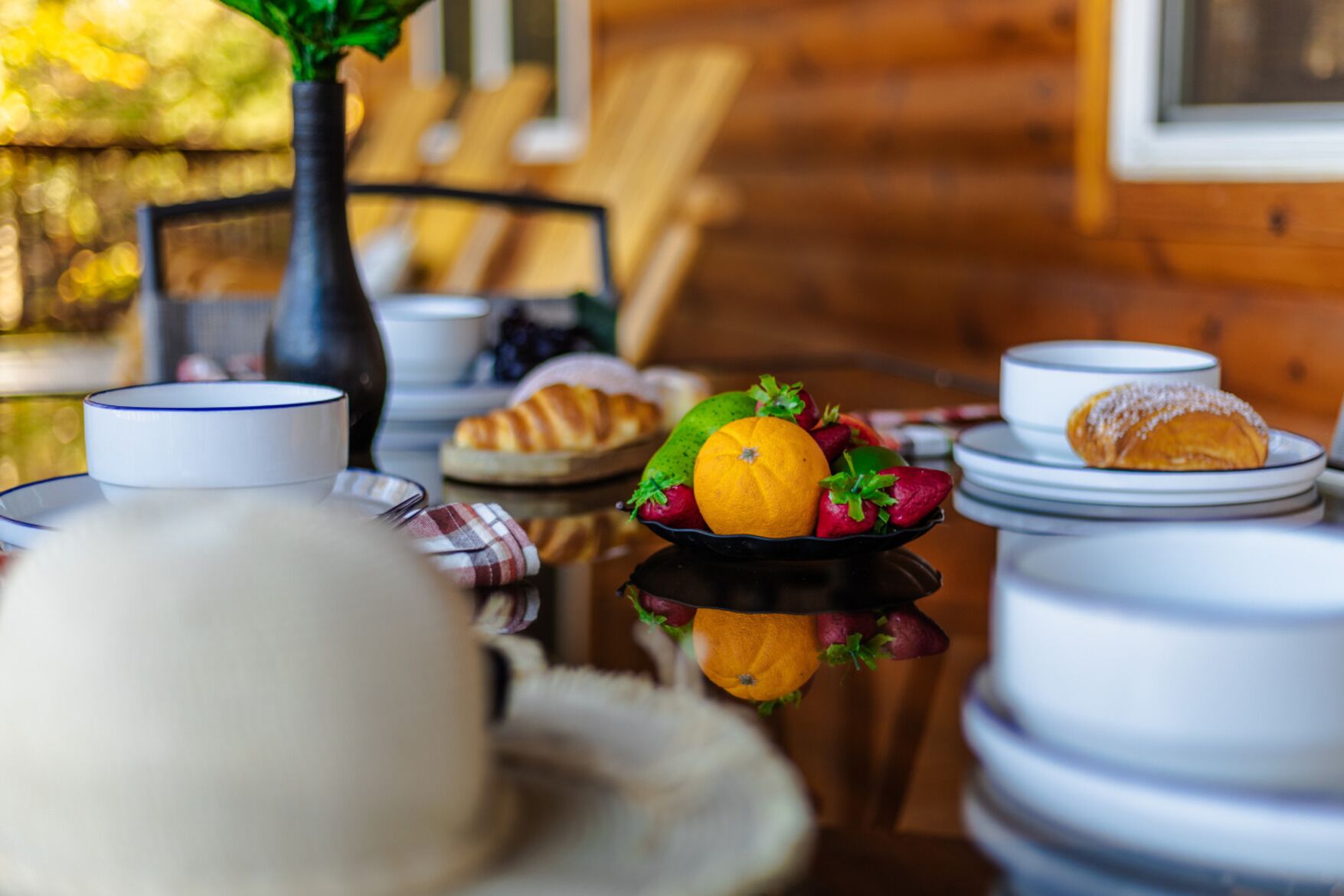 A dining table with plates, bowls, and a fruit bowl containing strawberries, an orange, and a lemon.