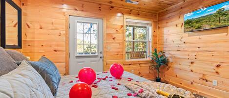 A cozy cabin room with a bed, two windows, a ceiling fan, and a view of the outdoors.