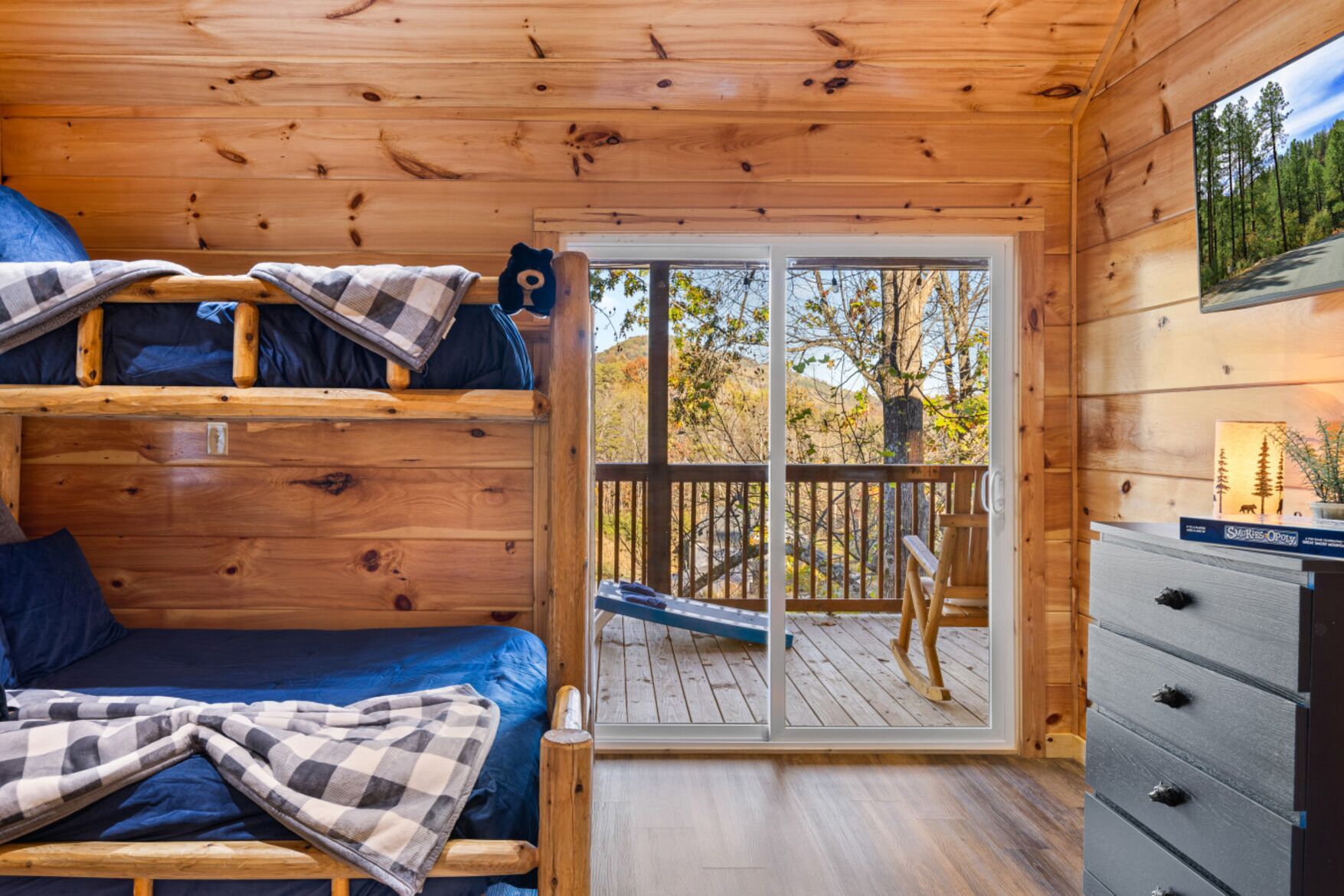 Eine Hütte mit Etagenbett, Schreibtisch und Blick auf einen Wald durch eine Glastür.