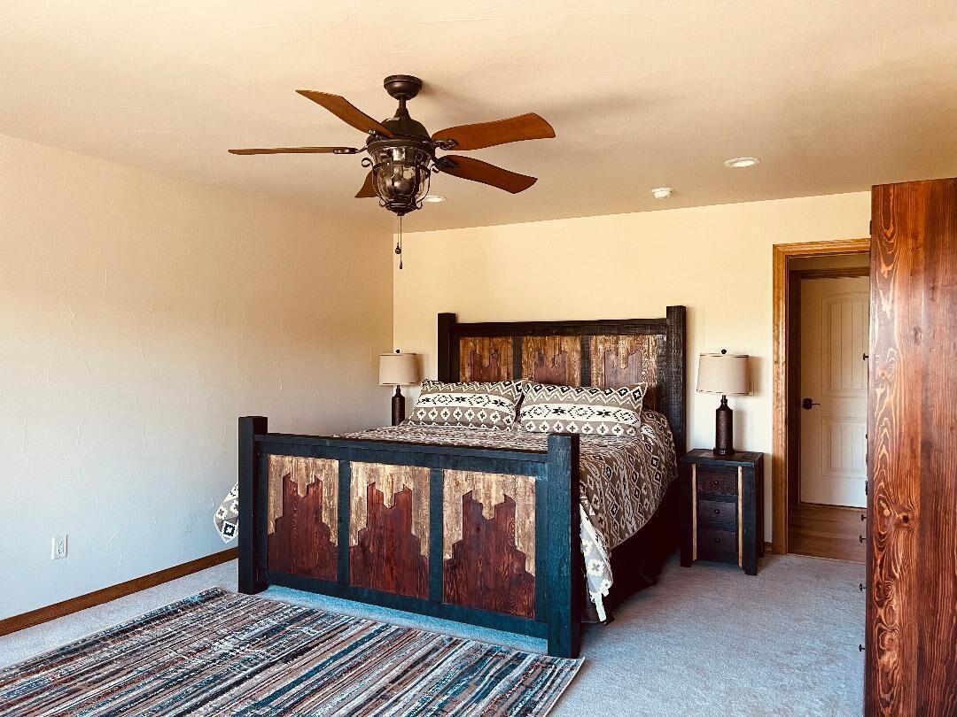 A bedroom with a bed, a ceiling fan, a nightstand, and a door.