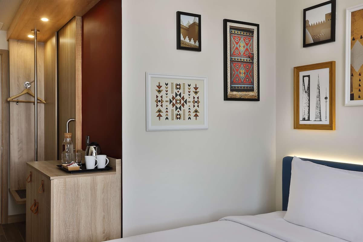 Ein Hotelzimmer mit Bett, kleinem Schreibtisch mit Kaffeemaschine und Wandbildern.