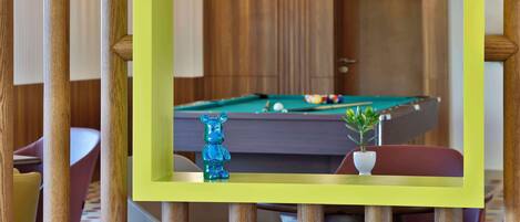 A pool table with a green frame, a blue bear figurine, and a small potted plant.