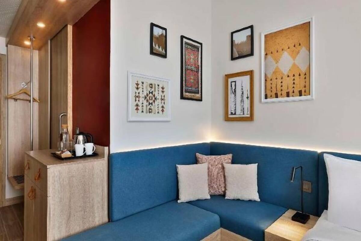 Ein Zimmer mit einem blauen Sofa, einem kleinen Tisch mit Wasserkocher und Tassen sowie gerahmten Kunstwerken an der Wand.