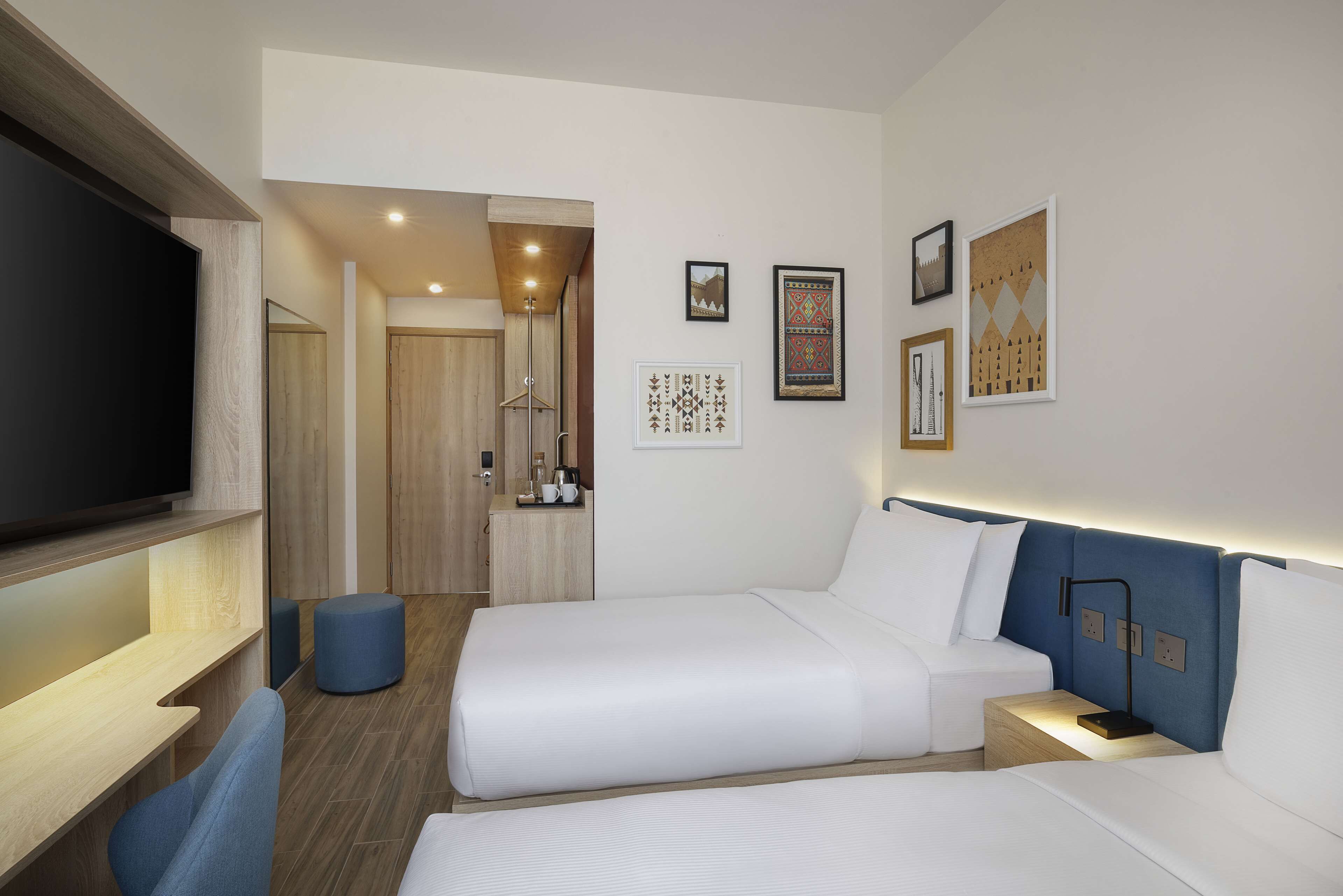 A hotel room with two beds, a TV, a desk, and a bathroom visible through an open door.