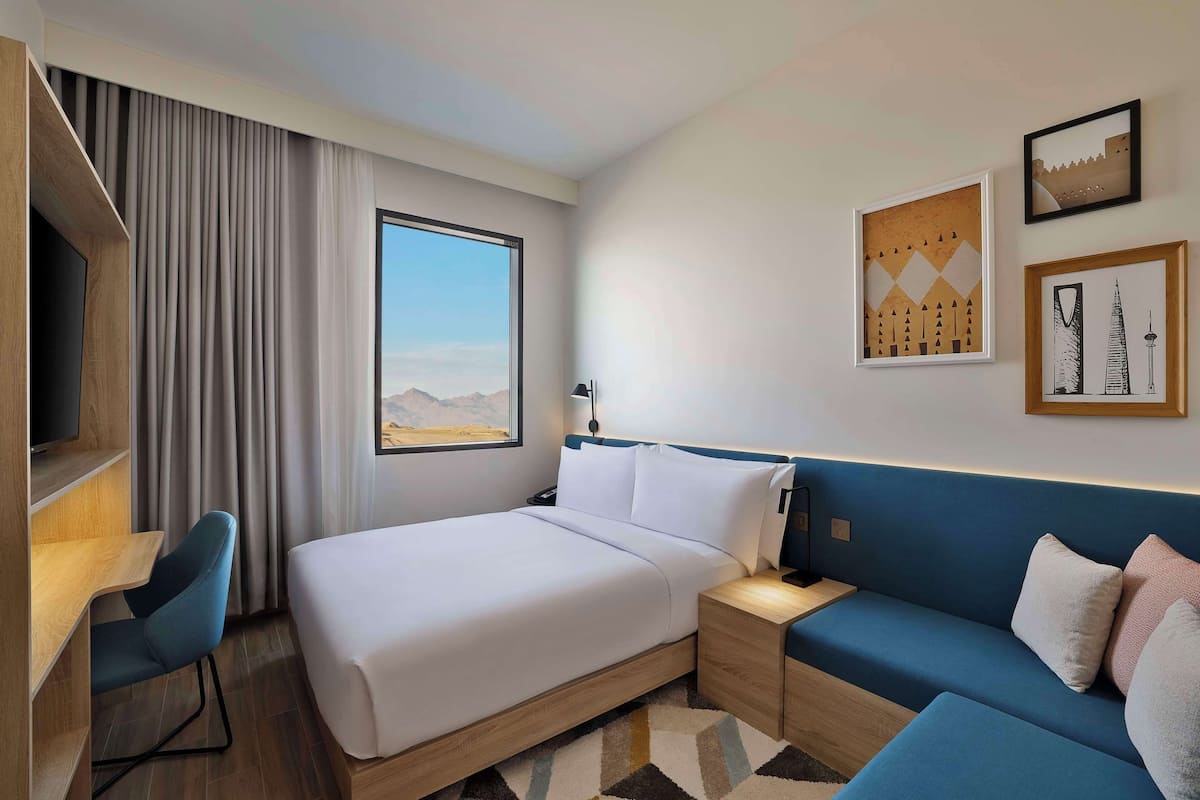 Ein modernes Hotelzimmer mit einem großen Bett, einem Schreibtisch, einem blauen Sofa und Blick auf die Berge.