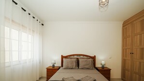 A bedroom with a bed, two bedside tables with lamps, a wardrobe, and sheer curtains. - Cristina Apartment - Near the Beach (Armação de Pêra)