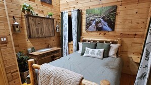 Una habitación acogedora de madera con una cama, un escritorio y un cuadro de un arroyo en el bosque.