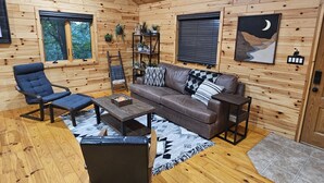 Interior acogedor de una cabaña con detalles de madera, un sofá marrón, un sillón azul y una mesa de centro de madera.