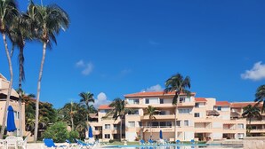 A resort pool area with clear blue water, lounge chairs, and palm trees. - Best Location 3BR Beachfront Condo with Ocean View (Puerto Aventuras)