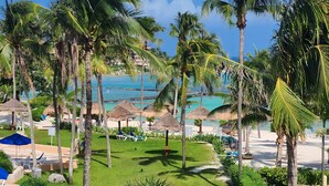 A tropical resort with palm trees, a beach, and thatched umbrellas. - Best Location 3BR Beachfront Condo with Ocean View (Puerto Aventuras)