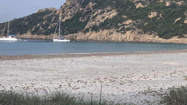 A beach with boats and rocky cliffs in the background.