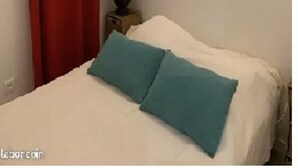 A room with a bed, a nightstand with a lamp, and a red curtain.