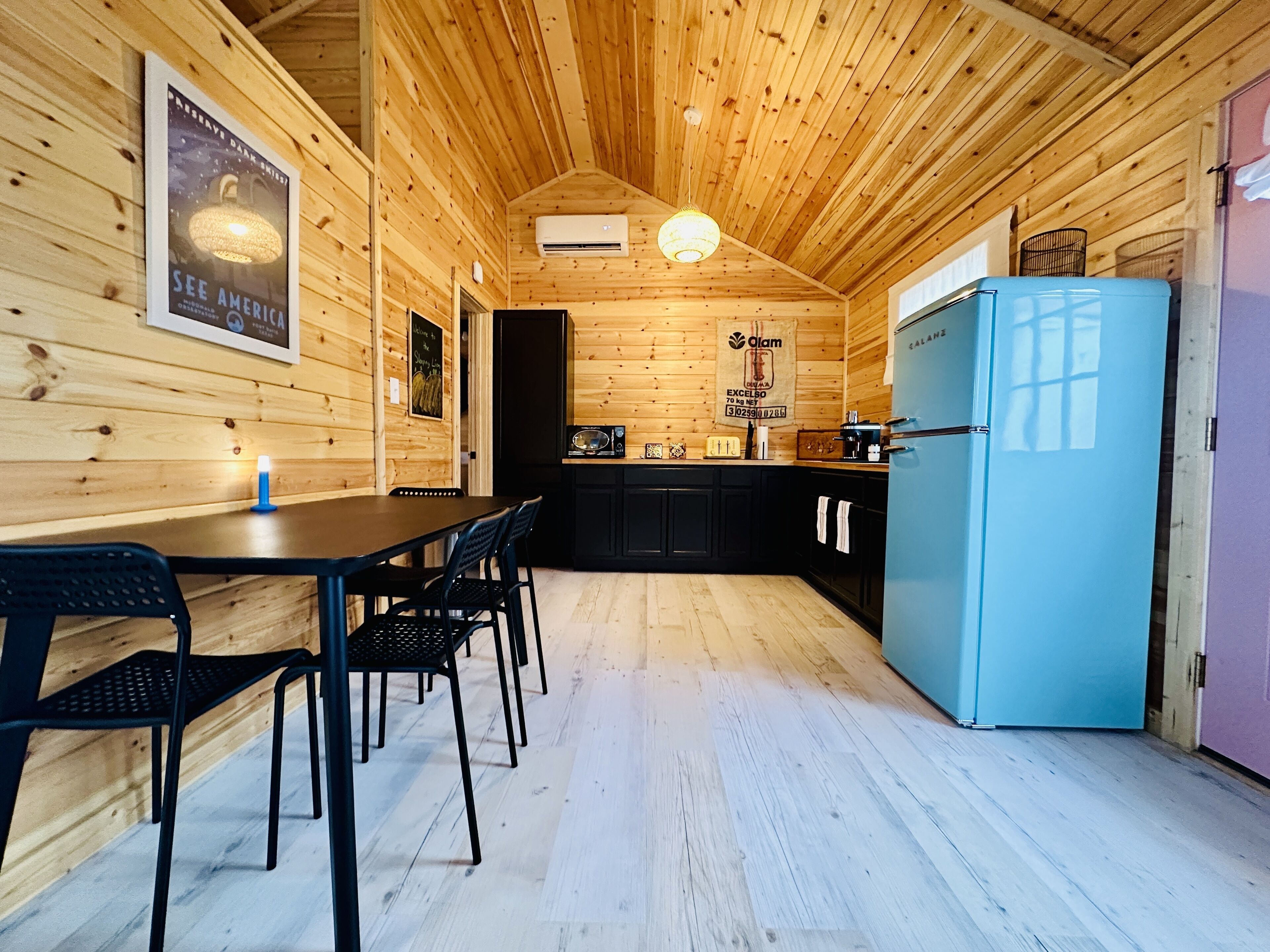 L’intérieur d’un chalet en bois comprend une table à manger, des chaises, un réfrigérateur bleu et un coin cuisine.