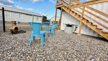 A patio area with a wooden staircase, a grill, and blue chairs.