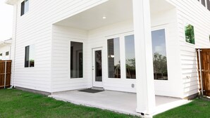A white two-story house with a covered patio and a fenced backyard.