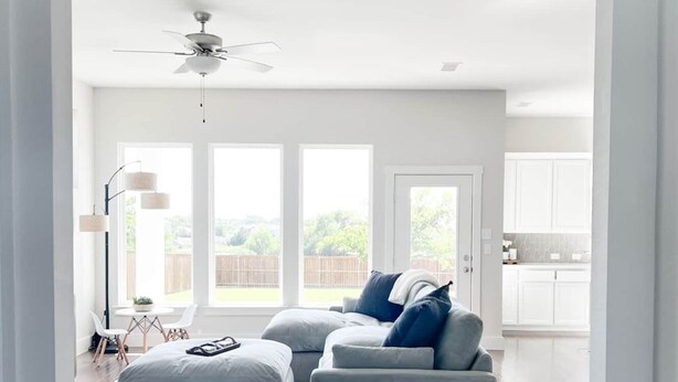 A spacious living room with a sectional sofa, a ceiling fan, and large windows offering a view of the backyard.