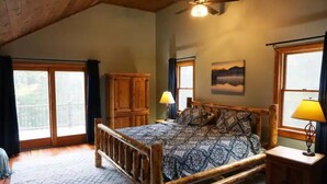 A spacious bedroom with a large bed, wooden headboard, and a ceiling fan. There is a window with curtains, a wooden cabinet, and a painting on the wall. - Spacious yet cozy house close to Gore Mountain

 (Johnsburg)