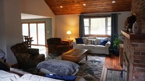 A cozy living room with a wooden ceiling, a fireplace, a sofa, a coffee table, and a lamp. - Spacious yet cozy house close to Gore Mountain

 (Johnsburg)