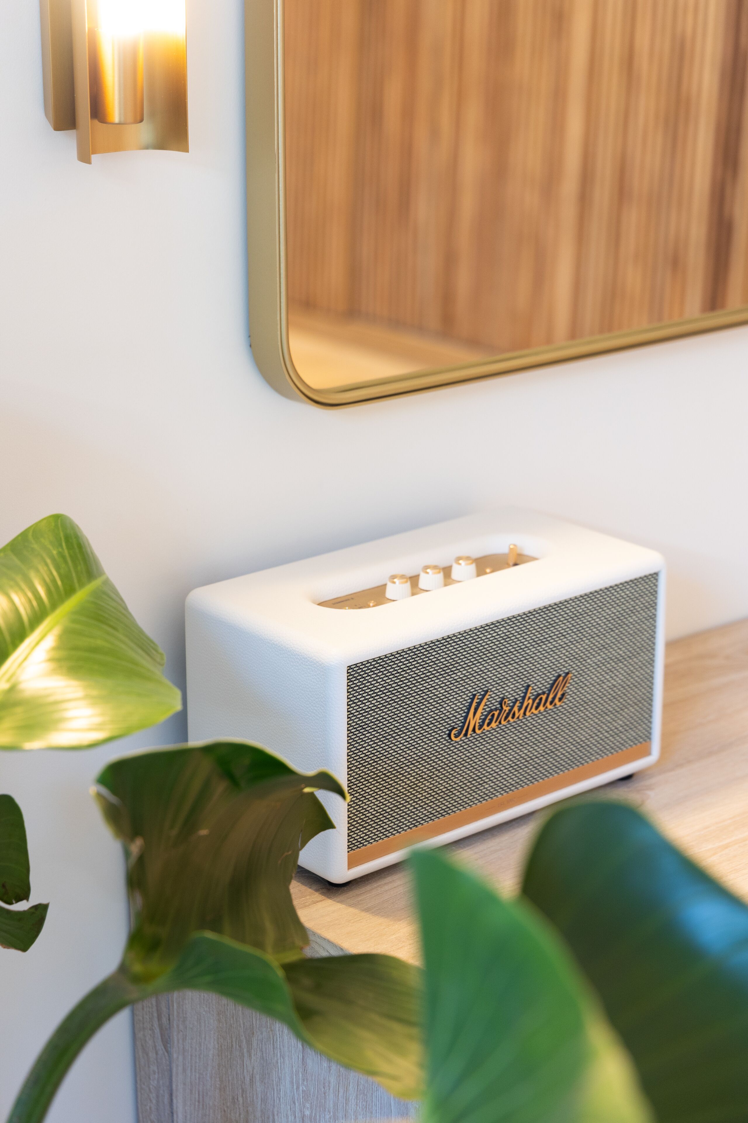Un altavoz blanco Marshall sobre una superficie de madera, con un espejo encima.