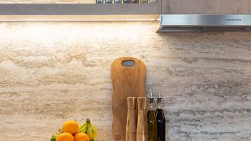 Une cuisine dotée de plans de travail en marbre, d’une planche à découper en bois, d’un saladier rempli de fruits et d’un ensemble de couteaux.