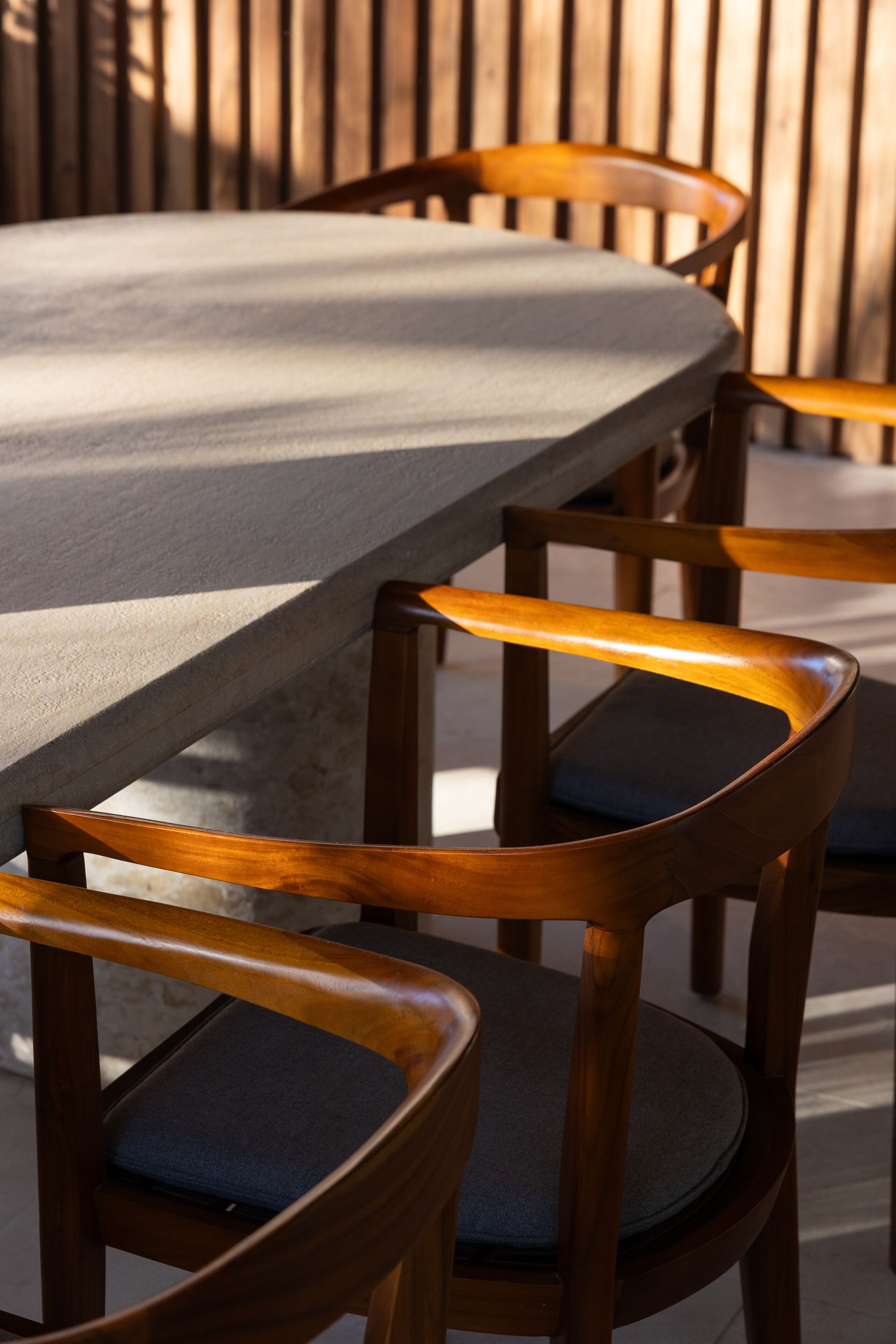 Une table à manger en bois, avec des chaises, installée à l’extérieur, avec une clôture en bois en arrière-plan.