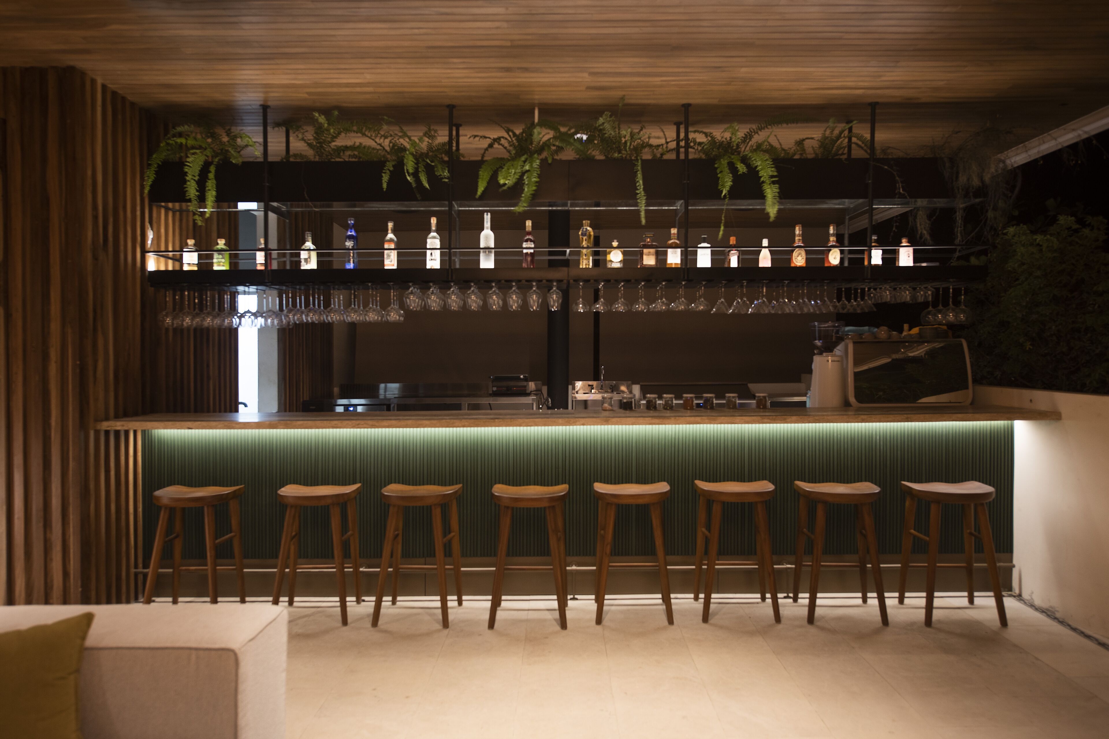 A bar area with wooden stools, a green bar counter, and hanging plants.