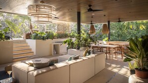 A modern outdoor living area with a sofa, dining table, and chairs, surrounded by potted plants and a staircase. - Silvestre Nosara, Hotel & Residences (Nosara)