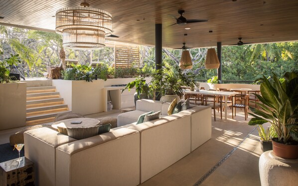 A modern outdoor living area with a sofa, dining table, and chairs, surrounded by potted plants and a staircase.