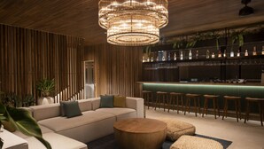A modern bar area with a wooden ceiling, a bar counter, stools, and a seating area with a sofa and ottomans. - Silvestre Nosara, Hotel & Residences (Nosara)