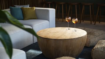 Una mesa redonda de madera con dos copas de vino, un sofá gris con cojines y una planta en primer plano.